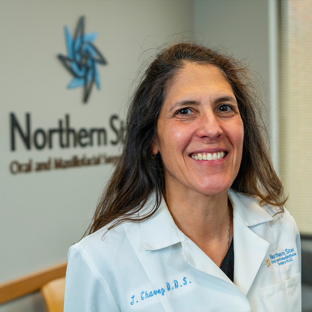The image shows a woman standing in front of a sign with the text NORTHERN STATE DENTAL AND MEDICAL SCHOOL smiling at the camera, wearing a white lab coat, and posing for a portrait.