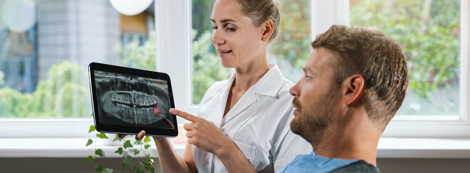 A digital tablet being used by a person in a medical setting with a woman in scrubs observing.