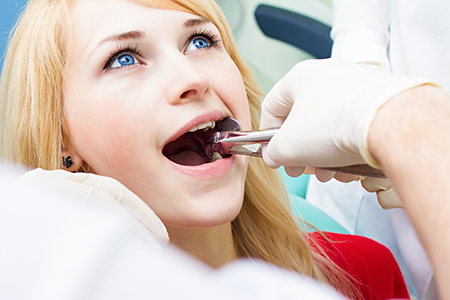 Woman receiving dental treatment with dentist in background.