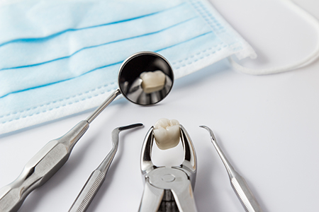 The image shows a collection of dental tools including a toothbrush, tweezers, and scissors placed on a blue cloth, with one tool having a small amount of white substance on its bristles, suggesting use in dental procedures.
